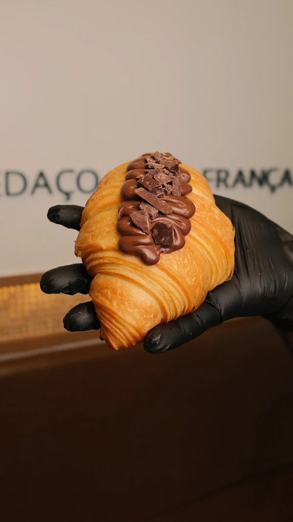 Croissant coberto com Nutella e lascas de chocolate, segurado por uma mão com luva preta