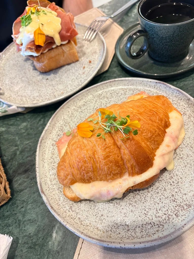 Croissant recheado e gratinado com queijo, com uma tartine poché ao fundo